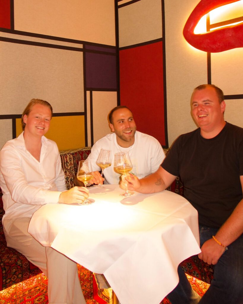 Two chefs in white jackets raising a glass of white wine at a table at BISOUS in De Pijp, Amsterdam