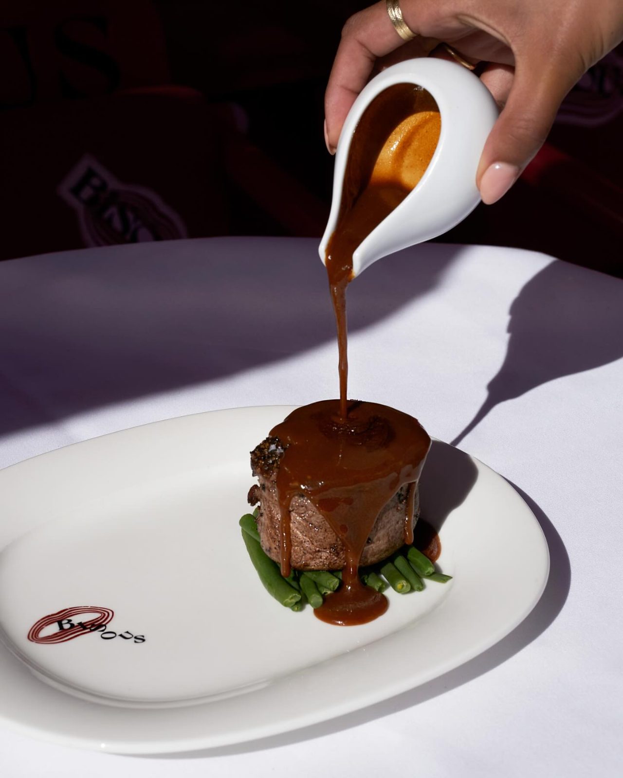 Peppercorn sauce being poured over the tournedos au poivre at the table at BISOUS in De Pijp, Amsterdam