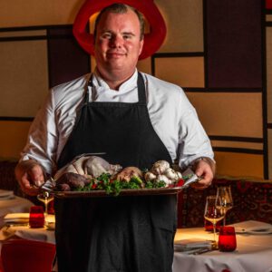 Chef Thomas Kooijman of BISOUS holding a tray of poultry, garlic and herbs in the dining room